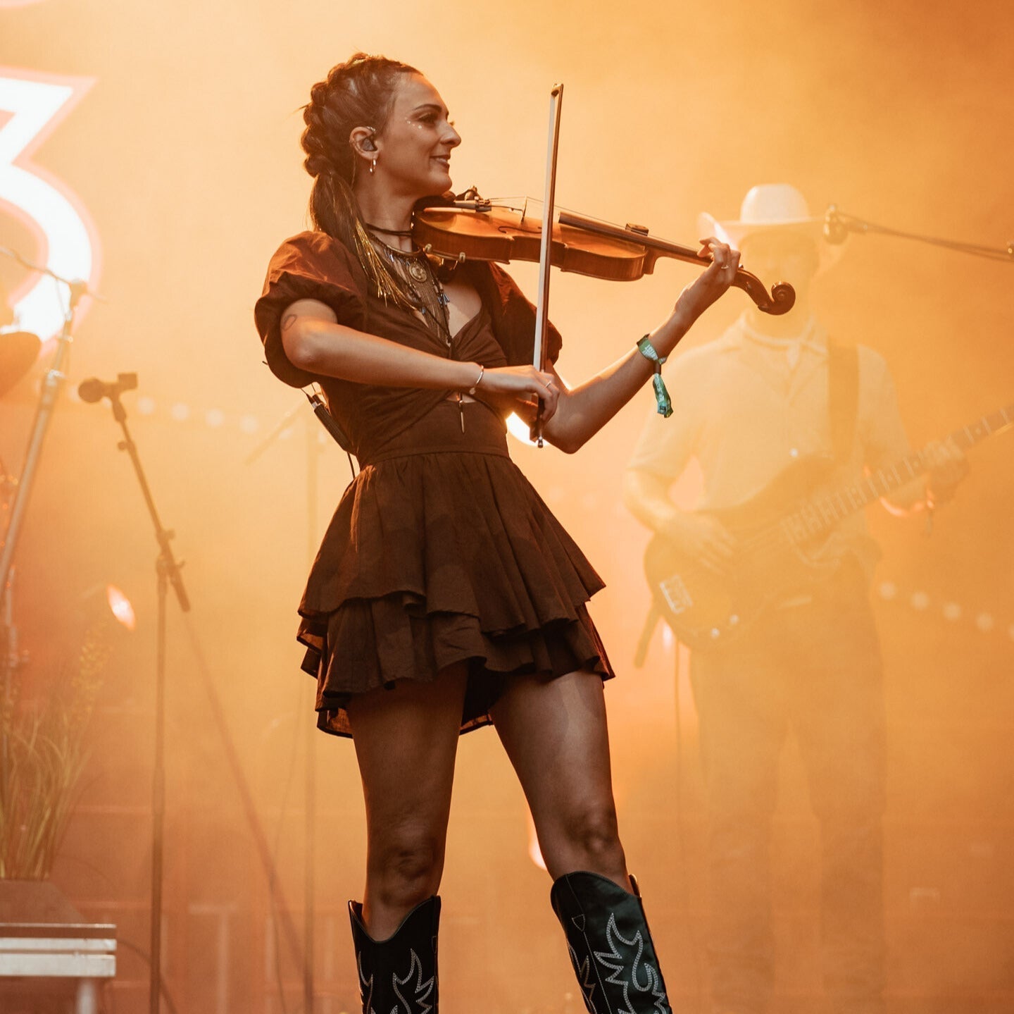 Kenzie Miracle playing fiddle with orange lighting behind her.