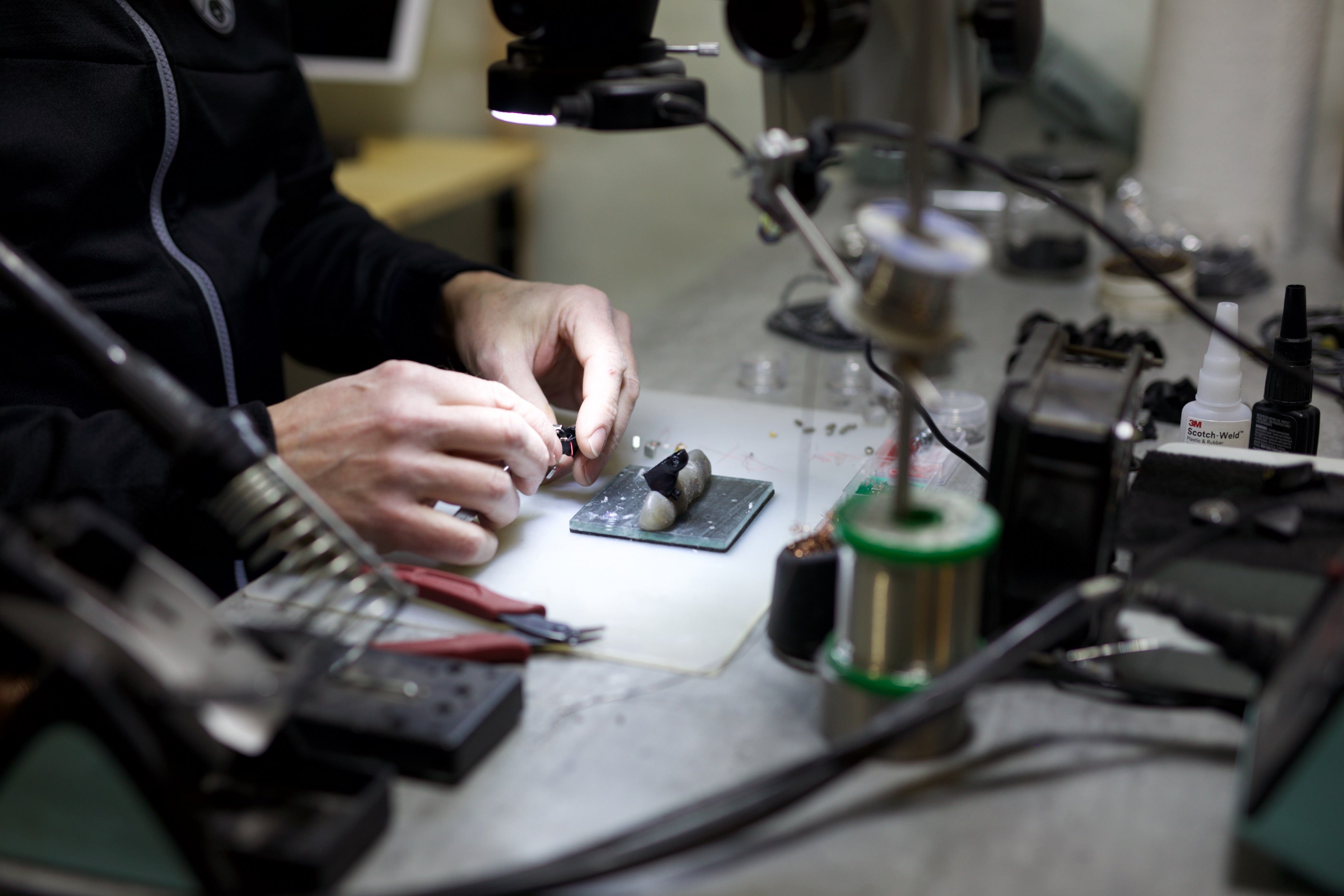 Man's hands building IEMs under a spotlight with small tools surrounding.