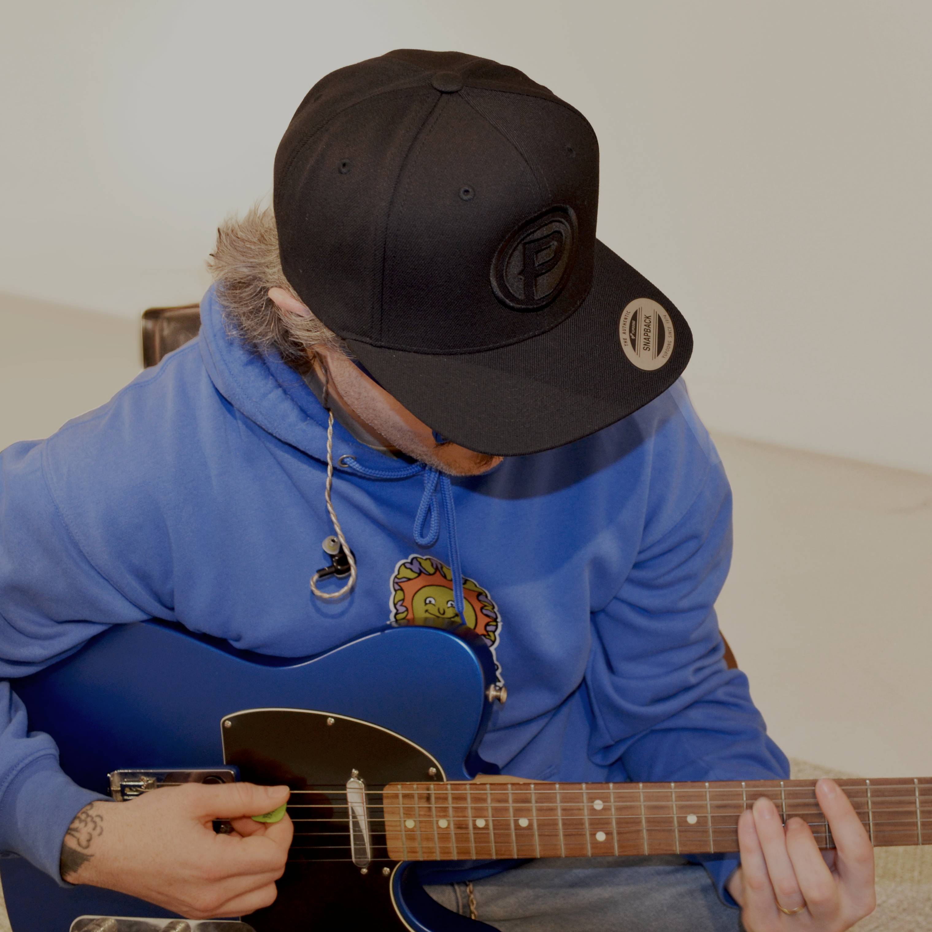 Person playing guitar wearing a blue hoodie and black Plunge cap.