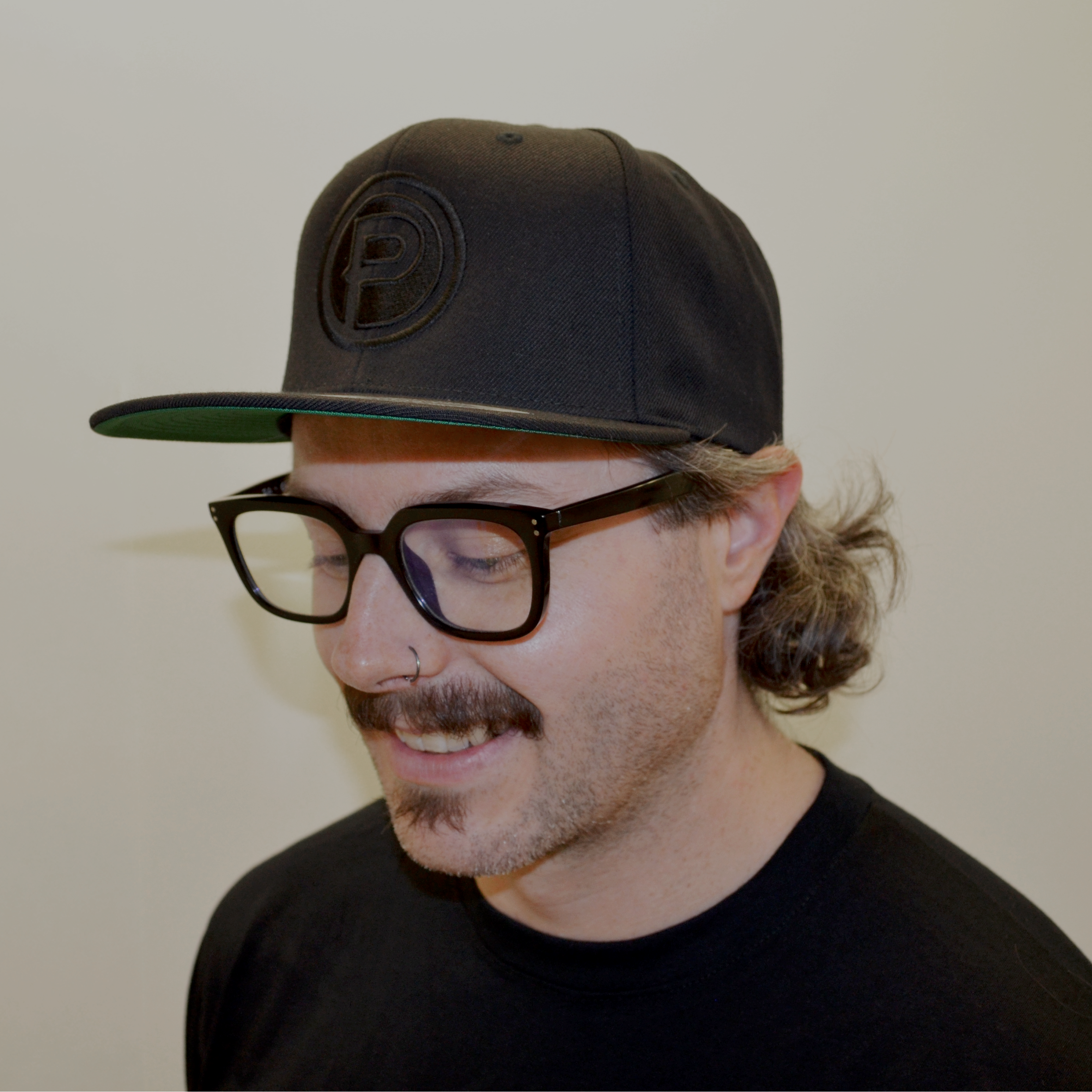 Man wearing a black Plunge Audio cap and glasses with a neutral background