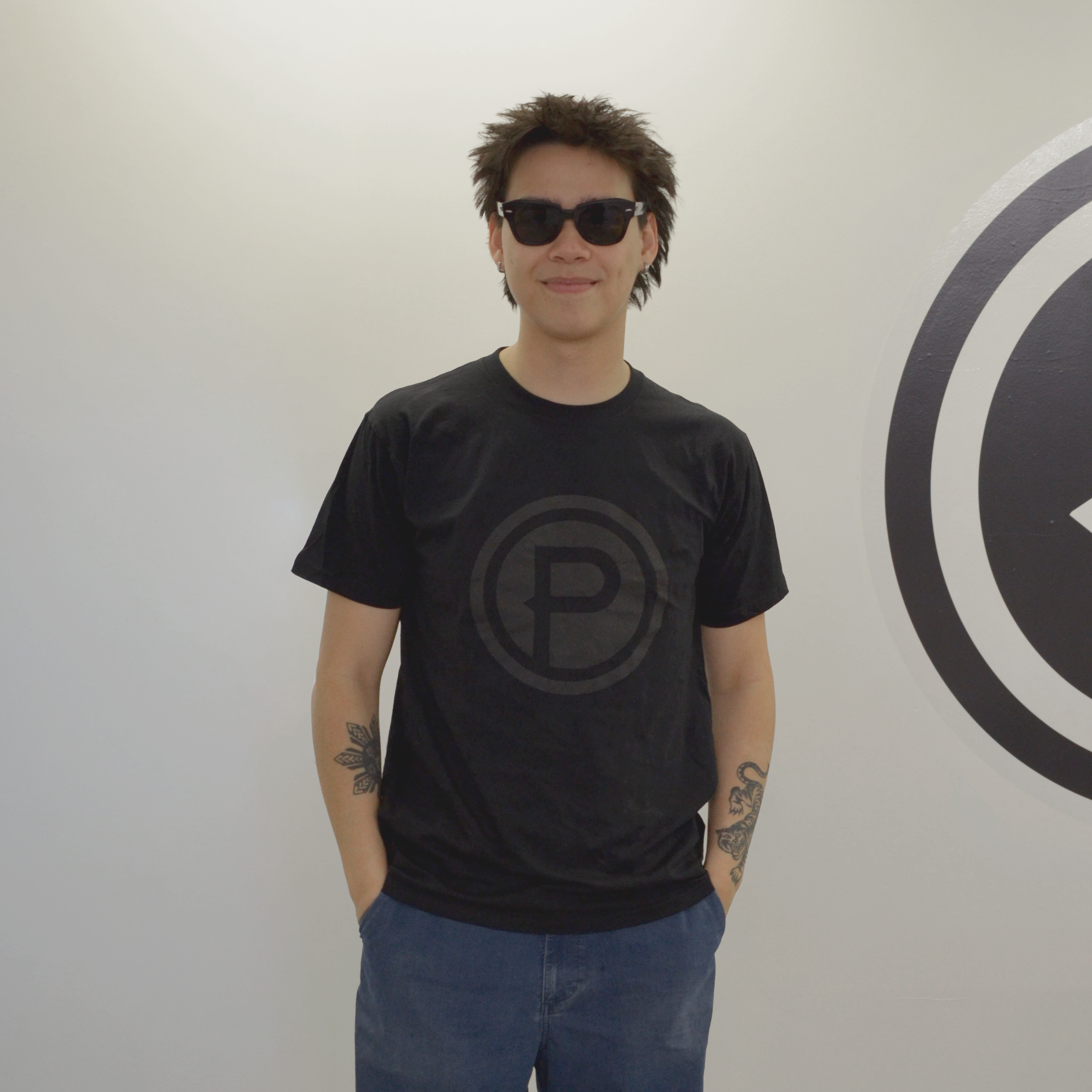 Person wearing a black Plunge t-shirt with a logo, standing in front of a white wall.