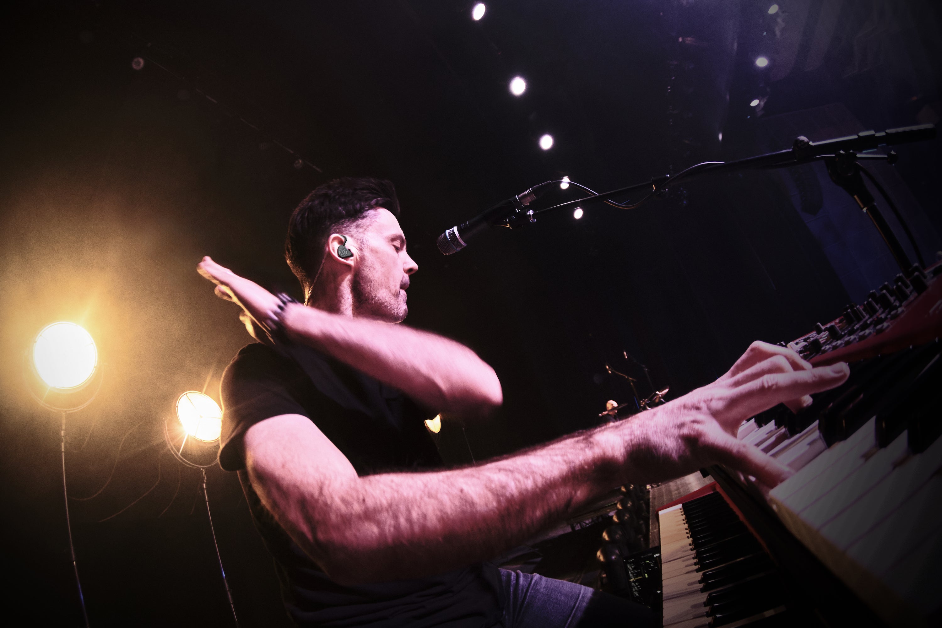 Man playing keyboard with mic under a spotlight.