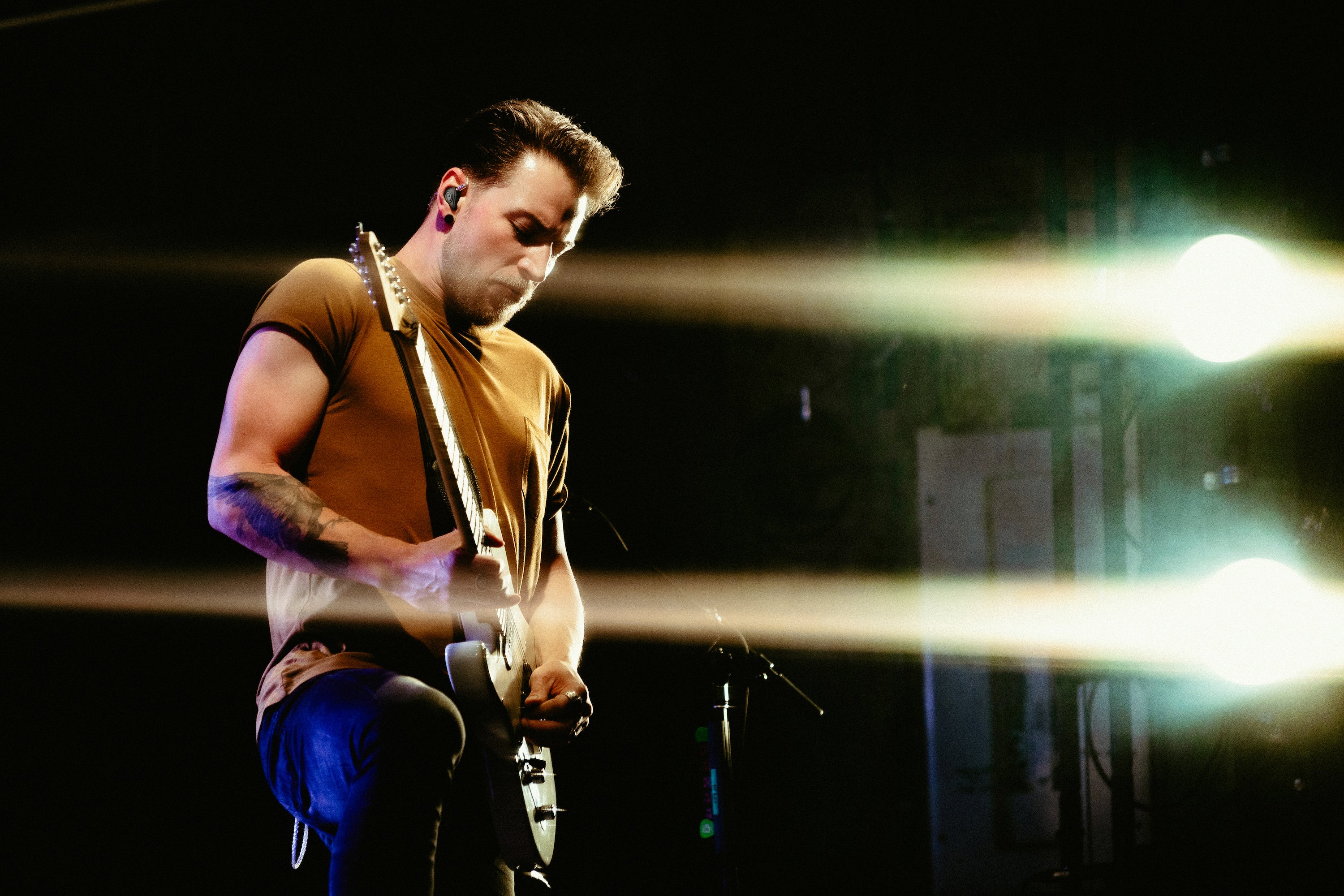 A man wearing IEMs and playing electric guitar during live performance.