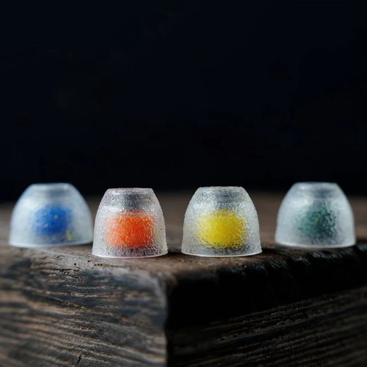 Four multi-coloured IEM tips sitting on wood shelf.