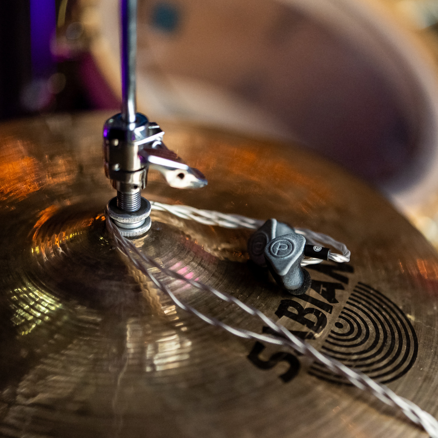 Plunge Audio IEMs resting on a gold cymbal, showcasing premium sound gear with a stylish aesthetic.