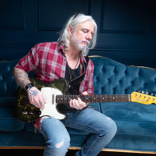 Musician Pete Lesperance playing guitar sitting on a couch.