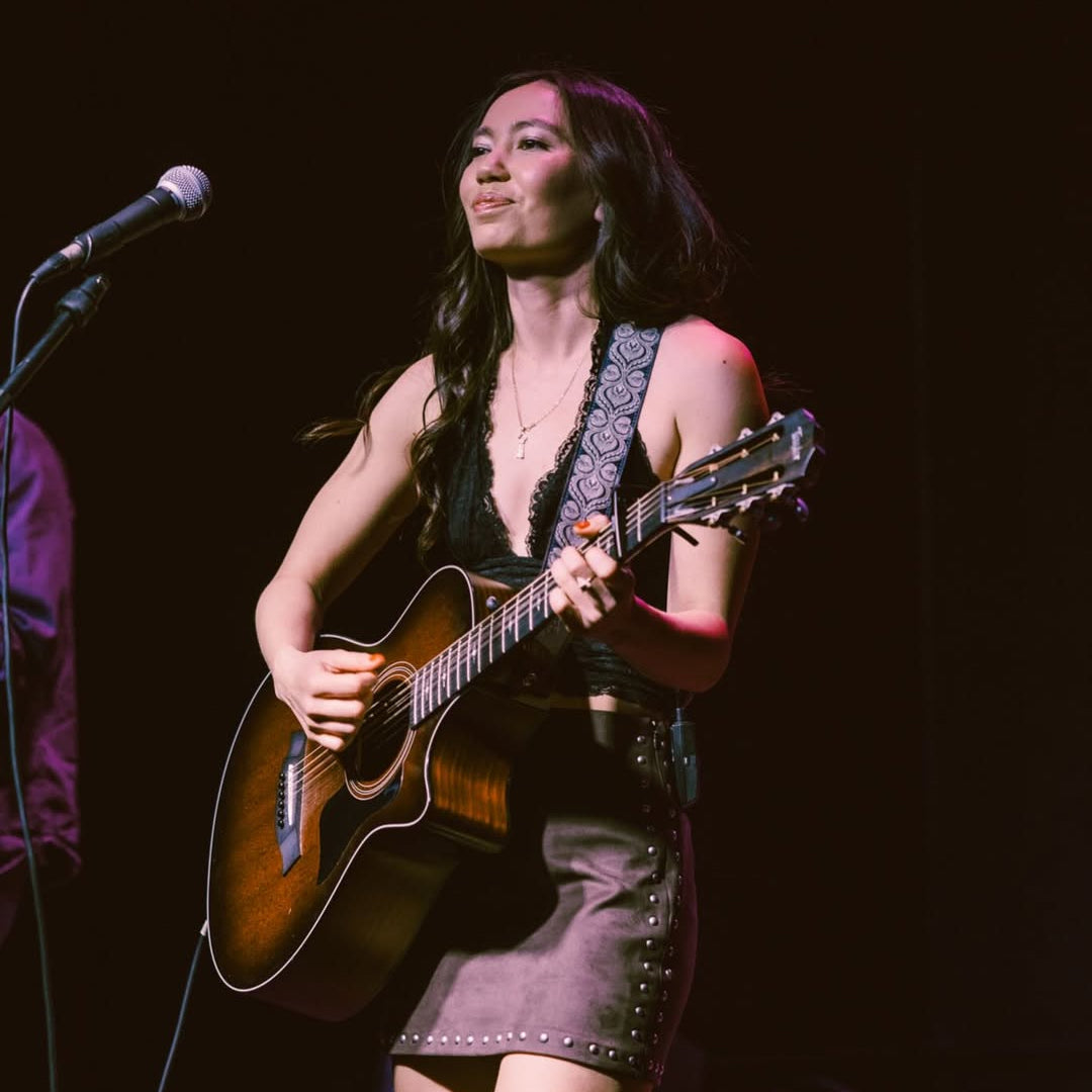 Woman playing guitar on stage with a microphone in front of her