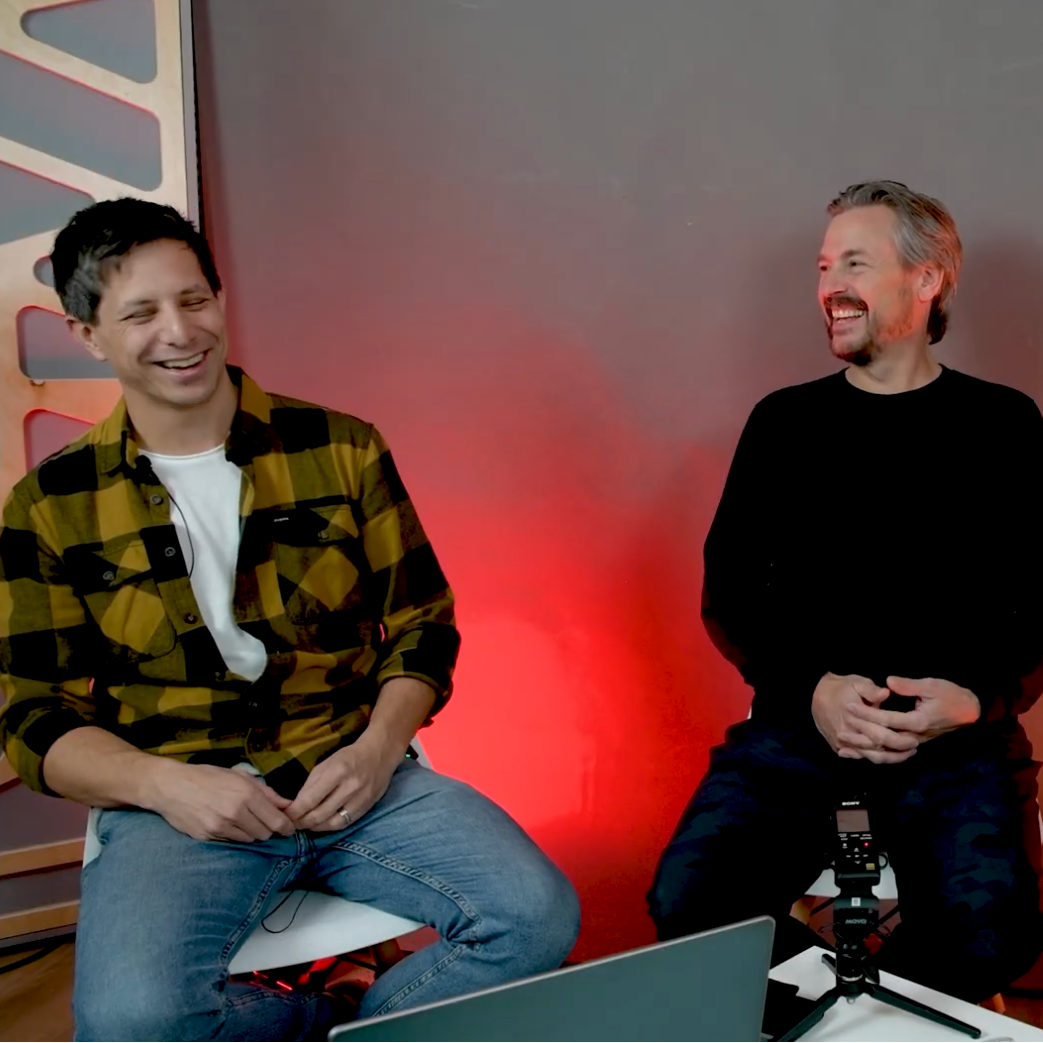 Justin Kudding and Simon Fisk are smiling with red backdrop.