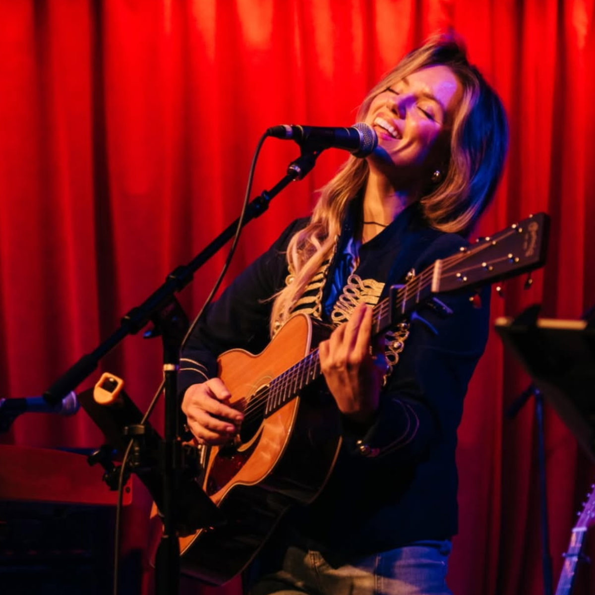 Therese Curatolo holds a guitar and sings on stage.