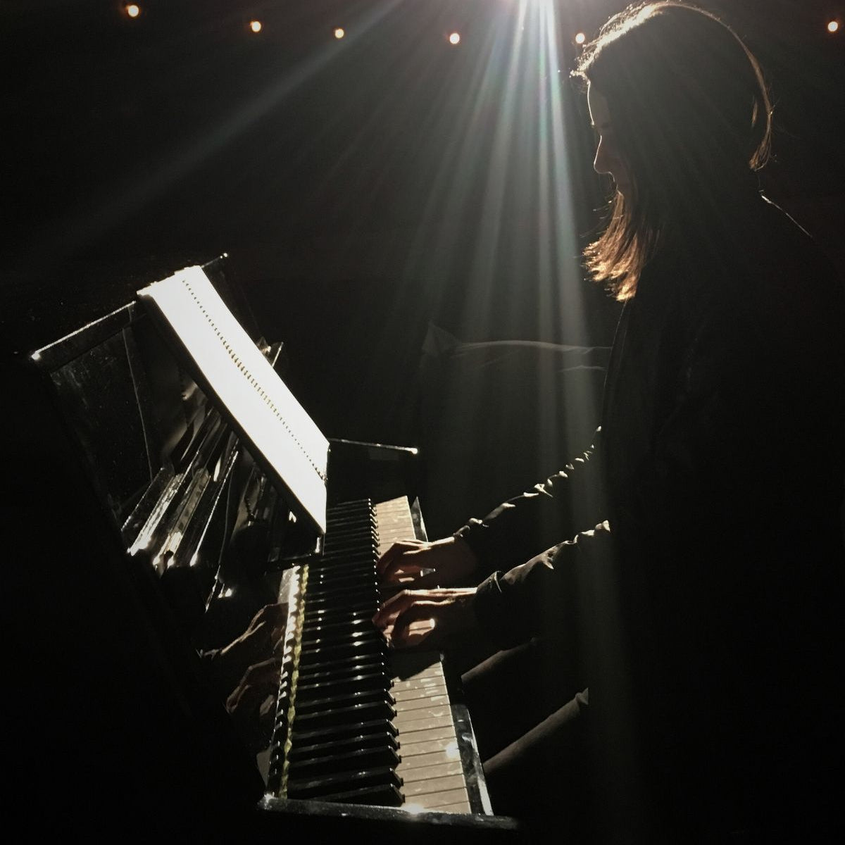Woman playing piano under spotlight.