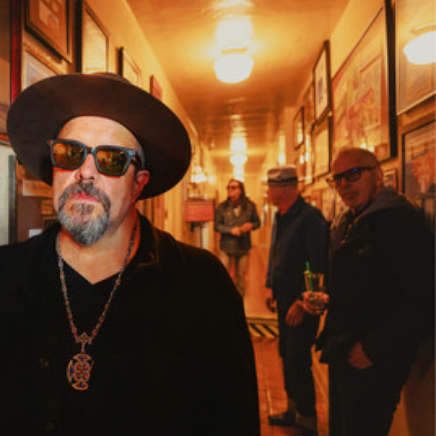 Four men from The Mavericks at varying depths wearing sunglasses and standing in a hallway.