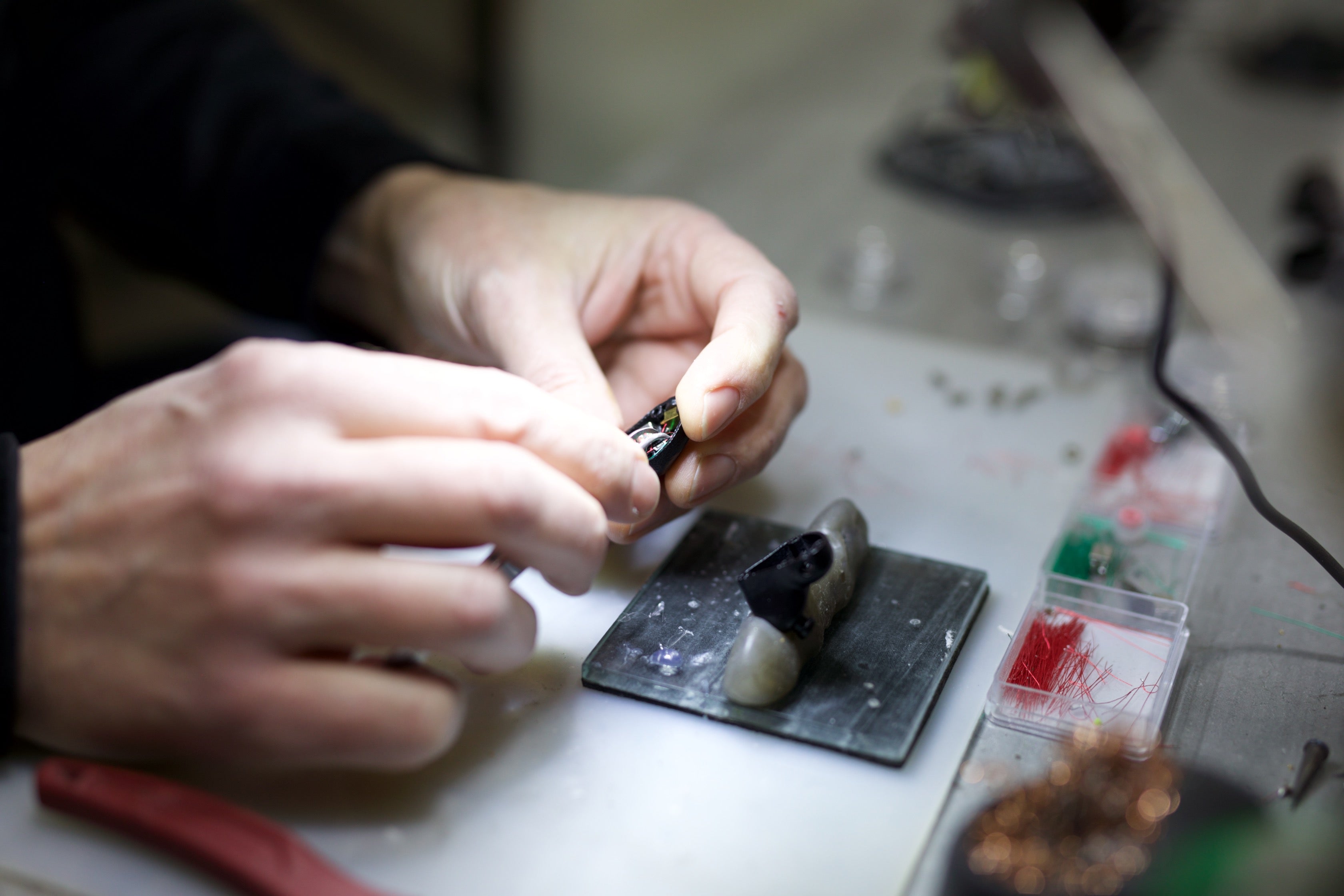 Man's hands building IEMs under a spotlight with small tools surrounding.