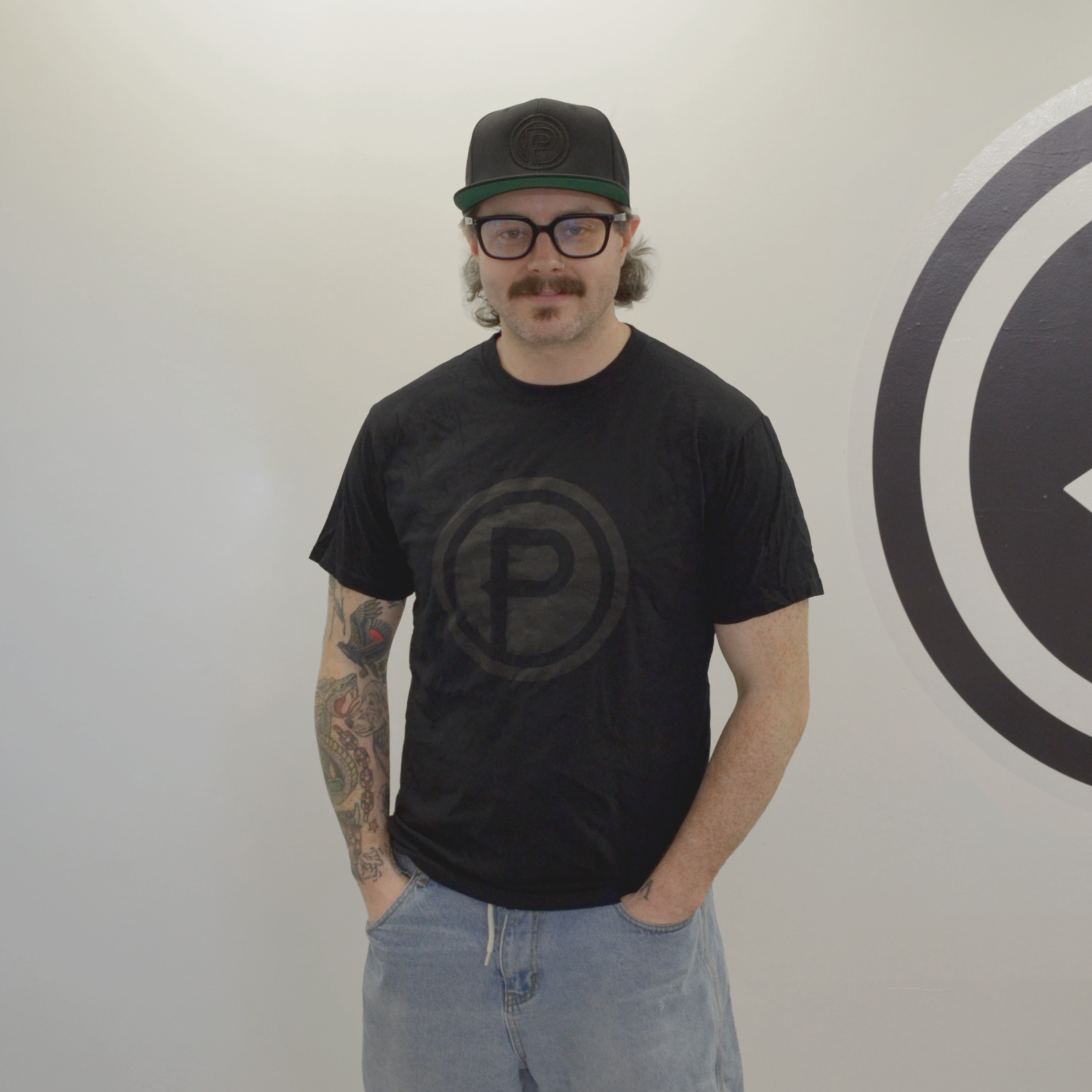 Man wearing a black Plunge t-shirt with a logo, light blue shorts, and a cap standing in front of a wall.