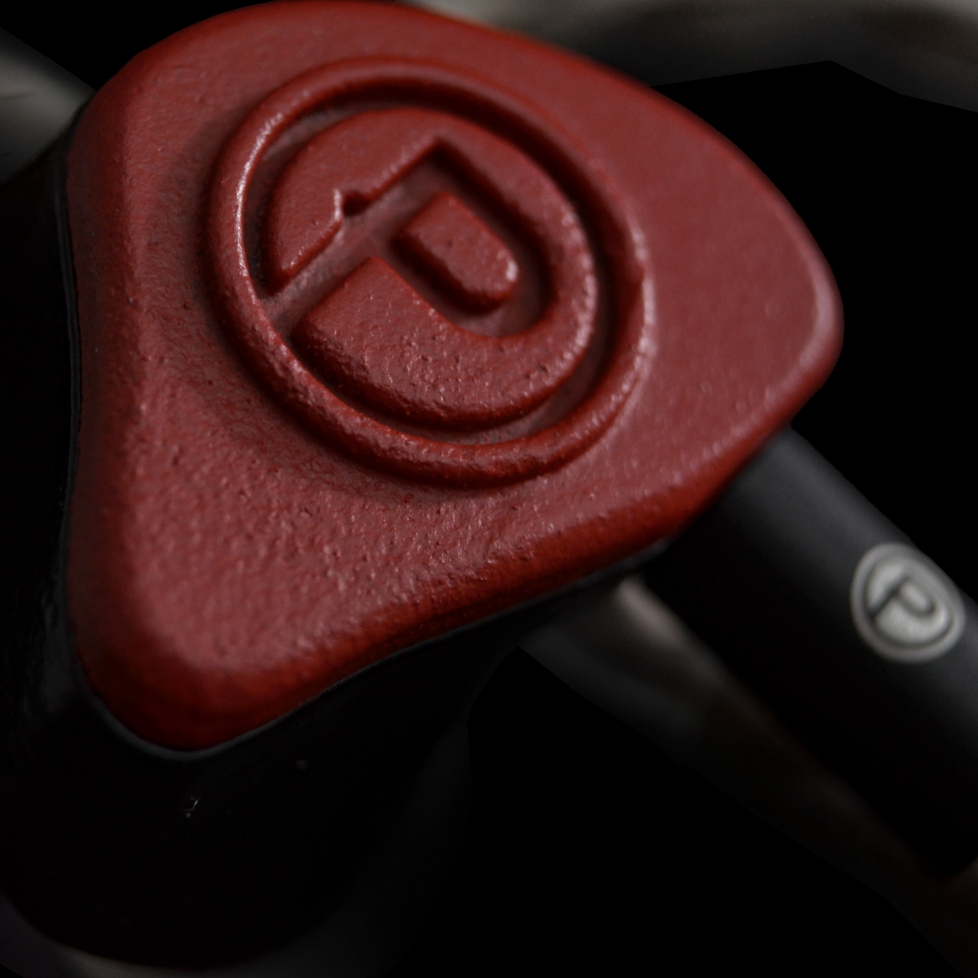 Close-up of a red IEM with a P logo on a dark background