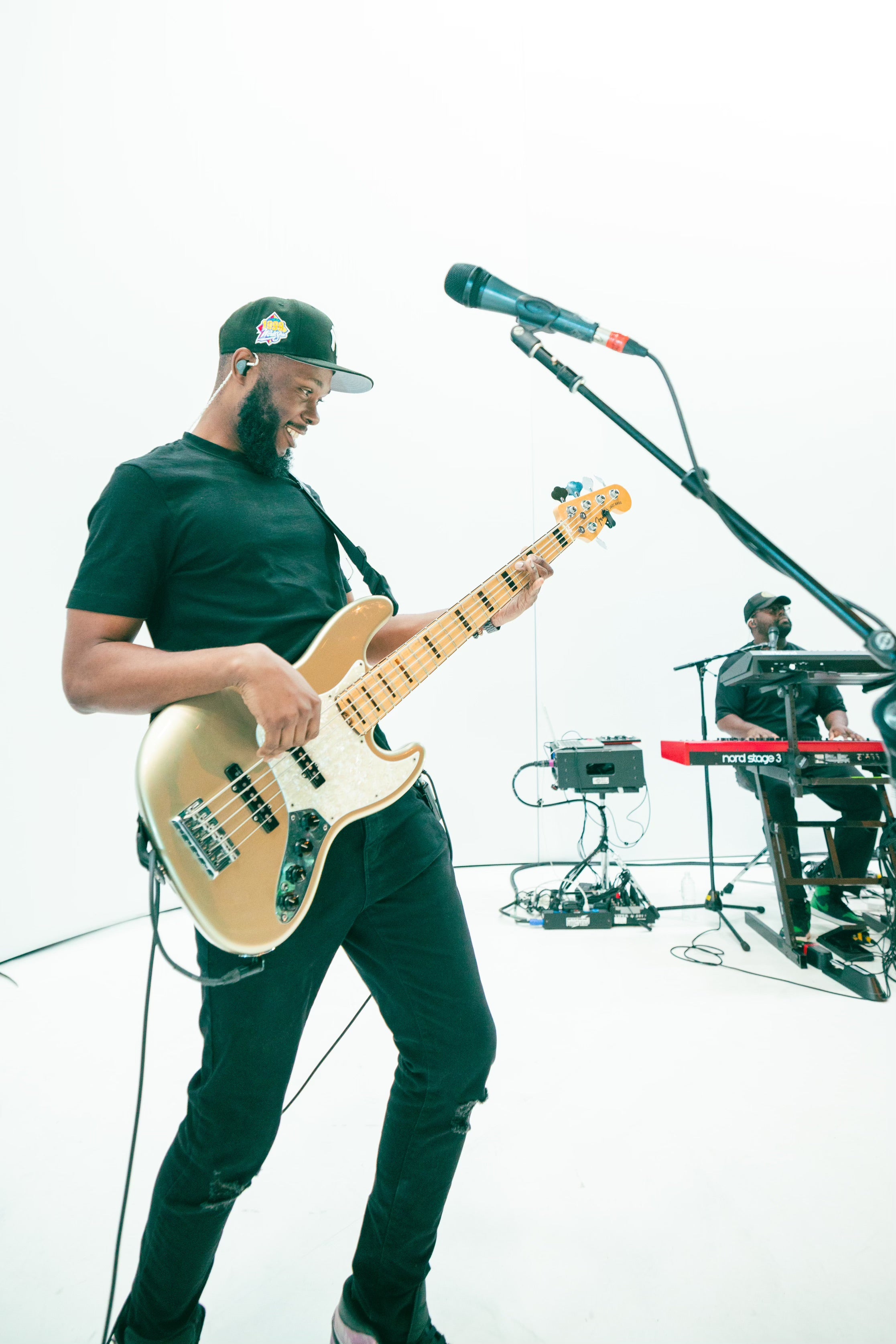 A man wearing IEMs and playing bass in a white room.